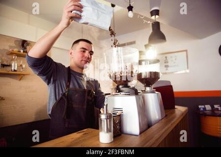 Der Barista macht Espresso im Café. Barista mahlt Bohnen mit Kaffeemaschine. Kaffeemühle Mahlen gerösteten Bohnen in Pulver. Stockfoto