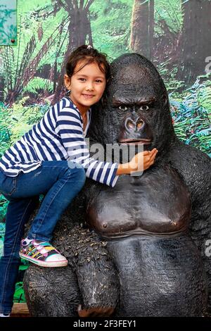 Junge englisch-thailändische Mädchen posiert für Fotos auf einer Gorilla-Statue Im Chester Zoo Stockfoto