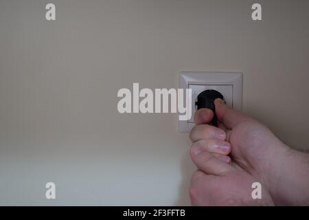 Männliche Hände ziehen ein schwarzes Netzkabel heraus, das eingesteckt ist In eine Steckdose Stockfoto