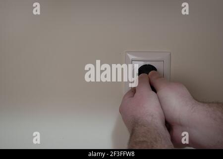 Männliche Hände ziehen ein schwarzes Netzkabel heraus, das eingesteckt ist In eine Steckdose Stockfoto