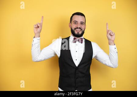 Junger Mann mit Bart mit Fliege und Weste Young Mann mit Bart trägt Fliege und Weste überrascht und Zeigt seine Finger zur Seite Stockfoto