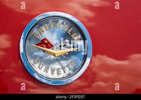 Chevrolet Corvette Hood Emblem mit Wolken Reflexionen auf leuchtend roten Fahrzeug Karosserie. Stockfoto