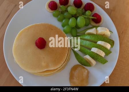 Die hausgemachten Pfannkuchen, Früchte und Honig auf einem weißen Teller Stockfoto