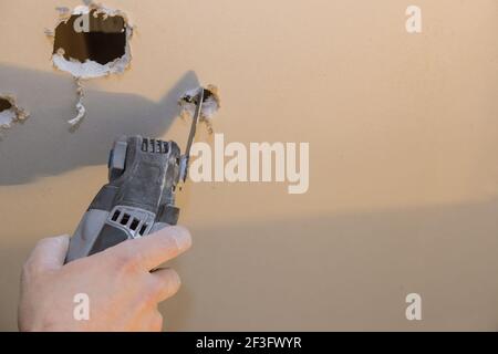 Mann schneidet Löcher auf Gipskartonplatten mit Hand elektrisch Elektrowerkzeuge Stockfoto