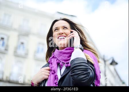 Eine junge spanische schöne Frau, die am Telefon und spricht Lachend mit einem leuchtend violetten Schal Stockfoto