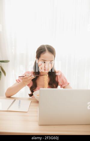 Weibliche Angestellte hält Essstäbchen essen Instant Nudel am Arbeitsplatz in Heimbüro Stockfoto