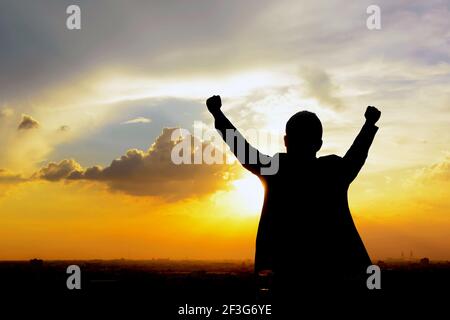 Silhouette eines Mannes, der seine Arme im Hintergrund des Dämmerhimmels hebt - Erfolg, Erfolg & erfolgreiche Konzepte Stockfoto