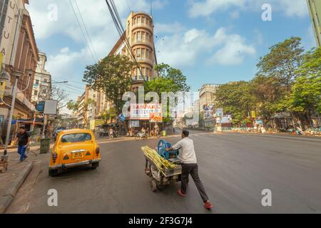 Verkäufer mit einem Zuckerrohr-Saftwagen auf der Stadtstraße mit Blick auf Bürogebäude in Chandni Chowk Bereich von Kalkutta, Indien Stockfoto