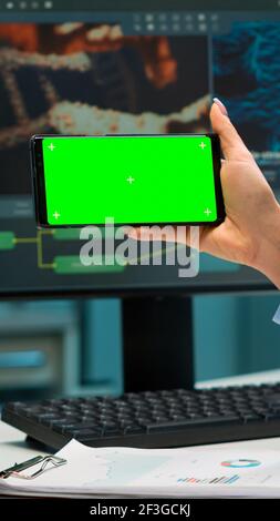 Nahaufnahme der Wissenschaftlerin Frau hält Smartphone mit grünem Mockup in modern ausgestatteten Labor. Team von Mikrobiologen tun Impfstoffforschung Schreiben auf Gerät mit Chroma-Taste, isolierte Anzeige. Stockfoto