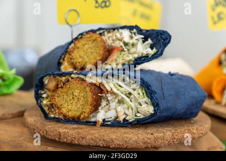 Falafel-Sandwich in flachem grünem Brot gerollt. Veganes Sandwich in Lavaschbrot mit Gemüse und frittiertem Ball oder Patty-förmigen Fritter aus grou Stockfoto