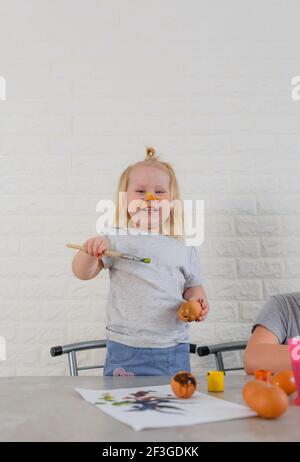 Ein kleines Mädchen in Farbe geschmiert lernt Eier zu malen Für die Osterferien Stockfoto