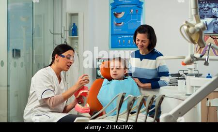 Stomatologe erklärt die richtige Zahnhygiene mit Präsentation Zähne Skelett, Extraktion einer Masse aus ihm. Zahnarzt erzählt, um Kind das Verfahren hält Probe des menschlichen Kiefers in Stomatologie Büro. Stockfoto