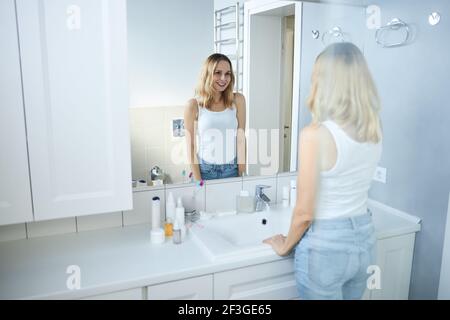 Charmante Frau, die im Spiegel im Badezimmer Stockfoto