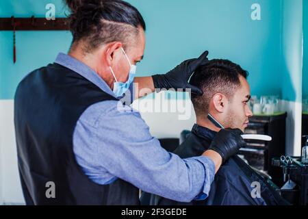 latein Mann Stylistin mit Gesichtsmask schneiden Haare zu einem Kunden In einem Friseurladen in Mexiko-Stadt in Coronavirus-Pandemie Stockfoto