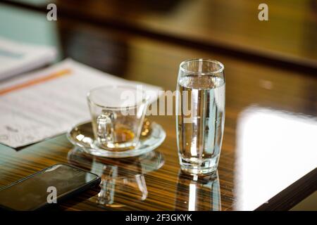 Shallow depth of field (selective focus) image with an empty coffee cup and a glass of sparkling water on the desk of a businessman during a corporate Stockfoto
