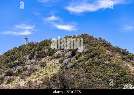 Spitze einer Bergkette, mit einem Signalsender, der hinter ihm gegen den blauen Himmel ragt, einschließlich mit ein paar dünnen, weißen Wolken. Stockfoto