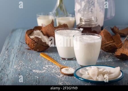 Ein Glas Kokosnussmoothies mit Kokosnuss. Coconut Smoothie vith Scheiben von frischer Kokosnuss und Flocken in Löffel auf Holzhintergrund. Stockfoto