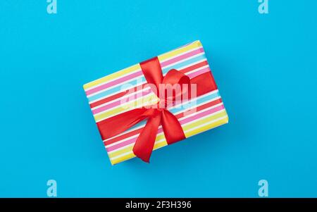Eingewickelte Geschenkbox mit roter Schleife auf blauem Papierhintergrund, Draufsicht Stockfoto