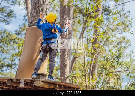 Glückliches Kind im Helm, gesunder Teenager Schuljunge, der an einem Sommertag in einem Kletterabenteuer-Park aktiv ist Stockfoto