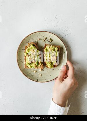 Weibliche Hand halten einen grünen Teller mit Avocado-Toasts mit Sprossen und verschiedenen Samen. Draufsicht. Speicherplatz kopieren Stockfoto