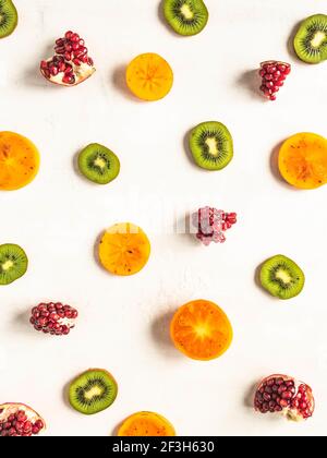 Bunte saisonale gesunde natürliche Frucht Hintergrund mit Kaki, Kiwi, Granatapfel Scheiben auf weißem Hintergrund. Draufsicht. Flach liegend Stockfoto