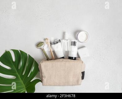 Reise Kosmetiktasche mit den notwendigen Mitteln, um die Haut der Frauen zu pflegen. Kosmetik, Massagegerät mit Kristallen, Trockenshampoo, Watteknospen, Zahnbürsten in einem Stockfoto