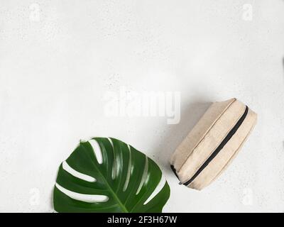 Öko Textil Kosmetiktasche und grünes Monstera Blatt auf grauem Hintergrund. Draufsicht. Speicherplatz kopieren Stockfoto