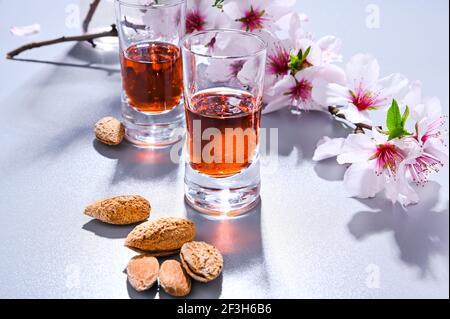 Mandellikör. Das traditionelle starke Getränk in italien, um das Abendessen zu vervollständigen, ist ein Likör aus Nüssen und Beeren. Ratafia, Alkohol in Schuss. Draufsicht auf dem Tisch und blühende Mandeln. Speicherplatz kopieren Stockfoto