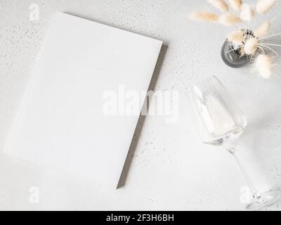 Weißer Zeitschriftendeckel Mockup, weißer Lagurus in Vase und Glas Weißwein auf hellgrauem Hintergrund. Draufsicht. Speicherplatz kopieren Stockfoto