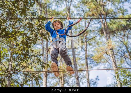 Glückliches Kind im Helm, gesunder Teenager Schuljunge, der an einem Sommertag in einem Kletterabenteuer-Park aktiv ist Stockfoto