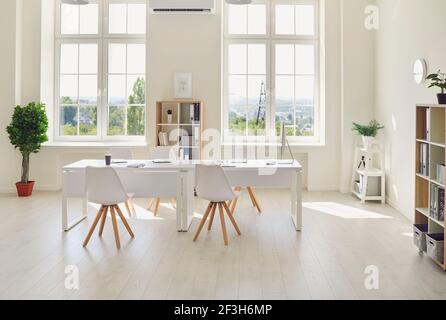 Interieur des gemütlichen hellen Bürozimmers mit großem Tisch, modernen Stühlen und großen Fenstern Stockfoto