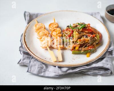 Garnelenspieß und asiatisches Gemüse braten auf weißem Teller. Stockfoto