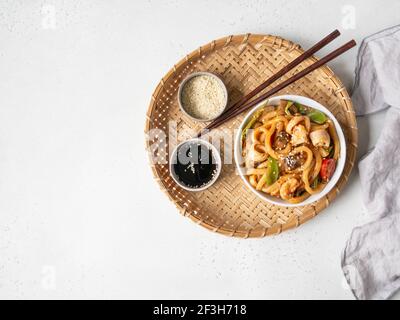 Udon Nudeln mit Meeresfrüchten und Gemüse in einem Wok in einer weißen Schüssel auf einem Weidenkorb gekocht. Draufsicht. Speicherplatz kopieren Stockfoto