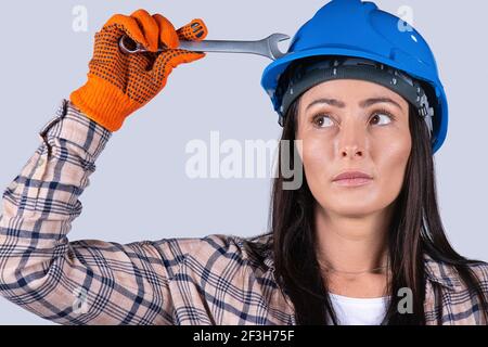 Porträt einer jungen Frau mit einem Automechaniker in einem Harthut und einem Schlüssel, der auf weißem Hintergrund zur Seite schaut. Stockfoto
