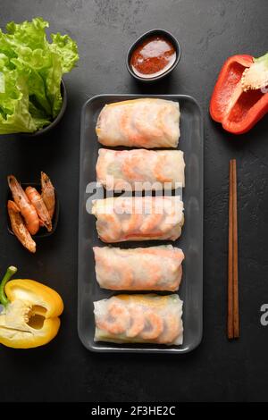 Asiatische Lebensmittel Frühlingsrollen mit Gemüse, Garnelen in Reispapier auf schwarzem Hintergrund. Blick von oben. Vertikale Ausrichtung. Stockfoto