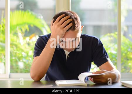 Junger Mann liest Buch mit der Hand auf dem Kopf Stockfoto