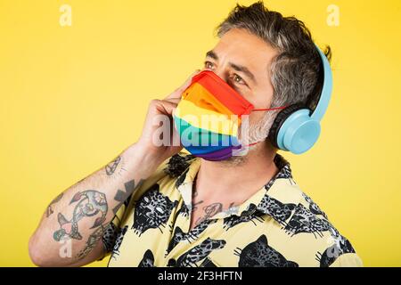 Mann hört Musik und trägt schützende Gay Pride Maske. Coronavirus-Lebensstil Stockfoto