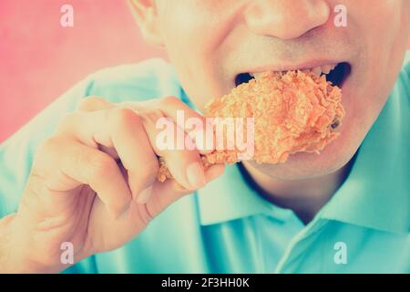 Ein Mann beißt frittiertes Hühnerbein oder Drumstick - Farbeffekt im Vintage-Stil Stockfoto