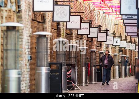 London, Großbritannien - 26. Februar 2021 - EIN Mann, der während der nationalen Sperre durch eine Reihe geschlossener Geschäfte am Camden Market läuft Stockfoto