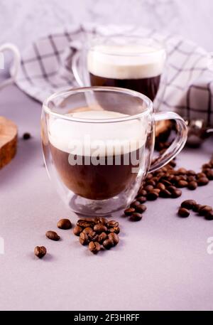 Transparenter doppelwandiger Glaskrug mit Kaffee und Milchschaum. Sofort Kaffee-Cocktail auf einem grauen Tisch und karierte Serviette. Stockfoto