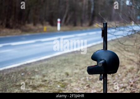 Ein Kreuz am Straßenrand mit einem Motorradhelm zum Gedenken an den tragischen Tod eines Motorradfahrers. Hergestellt an einem bewölkten Tag, weiches Licht. Stockfoto