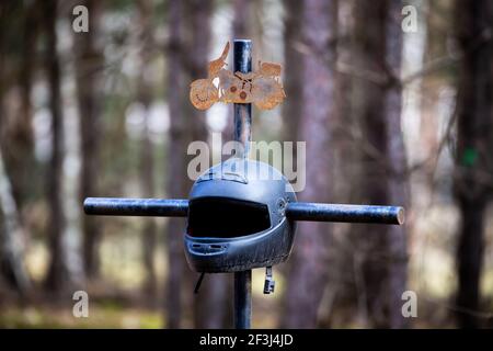 Ein Kreuz am Straßenrand mit einem Motorradhelm zum Gedenken an den tragischen Tod eines Motorradfahrers. Hergestellt an einem bewölkten Tag, weiches Licht. Stockfoto