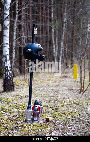 Ein Kreuz am Straßenrand mit einem Motorradhelm zum Gedenken an den tragischen Tod eines Motorradfahrers. Hergestellt an einem bewölkten Tag, weiches Licht. Stockfoto