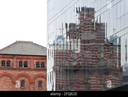 Kunstvolles Gebäude, das sich in der schwarzen Glasfassade des Mann Island-Bauwerks, Pier Head, Liverpool, widerspiegelt, neben einem renovierten roten backsteingebäude Stockfoto