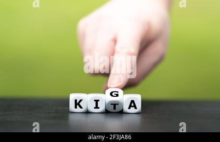 Hand dreht Würfel und ändert die deutsche Abkürzung KITA (Kindertagesstätte) zu KIGA (Kindergarten). Stockfoto