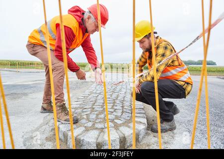 Zwei Arbeiter auf der Straßenbaustelle kontrollieren Pflastersteine Stockfoto