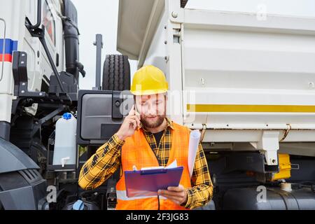 Bauarbeiter oder Bauleiter mit Checkliste und Smartphone in Vorderseite des Staplers auf der Baustelle Stockfoto