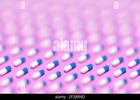 3D Abbildung weiß - blaue Kapseln, Tabletten mit Medizin in geraden Reihen auf einem rosa Hintergrund. Kapselmedizin Stockfoto