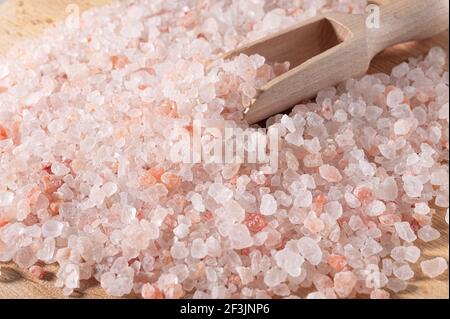 Rosa himalaya-Salz. Nahaufnahme Himalayan Pink Rock Salt in Holzlöffel auf schwarzem Hintergrund. Draufsicht. Haufen grobkörniges Salz Stockfoto