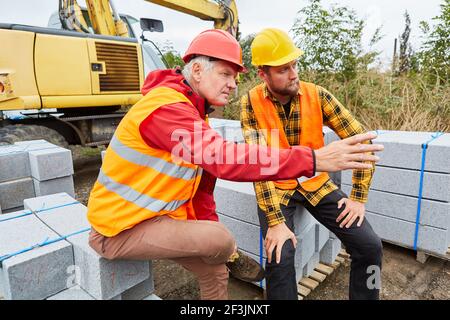 Zwei Bauarbeiter auf der Baustelle des Hausbaus Mit Baustoffen und Bagger Stockfoto